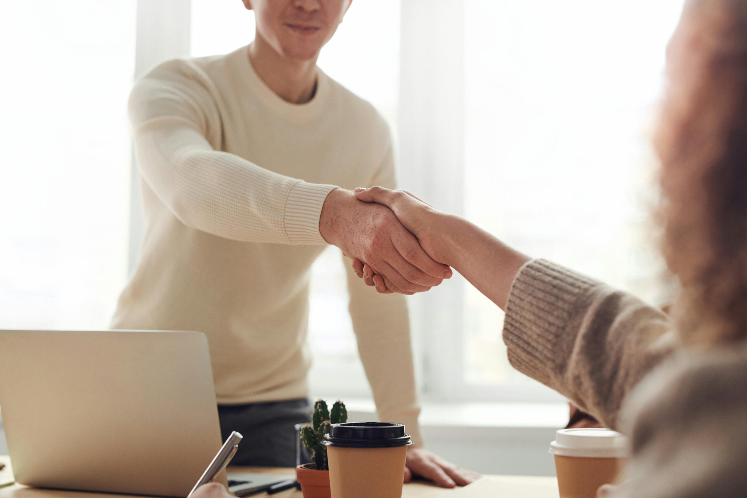 Close-up of professionals shaking hands over coffee in a modern office. Using CONNECT-X services.